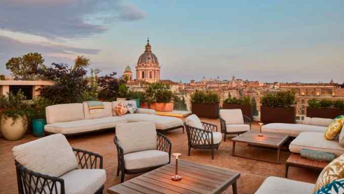 Beige and dark-wood furniture on the terrace of Bulgari Hotel Roma, looking over the Rome skyline