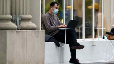 A mask-clad man works on his laptop in outdoors in Shanghai