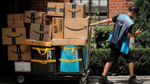 An Amazon delivery worker pulls a delivery cart full of packages