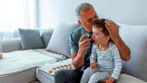 A caring father gives asthma medicine to his toddler son using an inhaler
