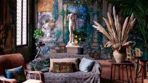 Tapestries on the walls, nude statuary, plants, sofas draped in textiles in a high-ceilinged room with huge window