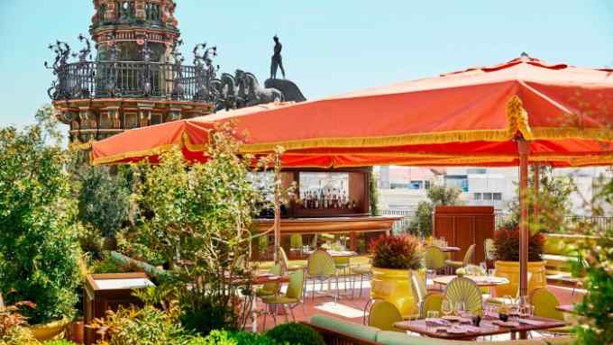 The rooftop terrace of Four Seasons Madrid’s Dani restaurant, with a large orange parasol over a table and the top of an ornate monument in the background