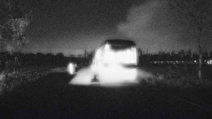 A grainy image of a bus illuminated at night with what seem like people standing near it