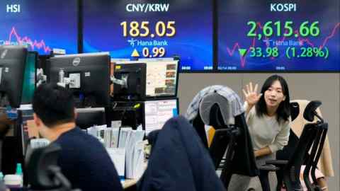 A currency trader gestures near screens showing the Korea Composite stock Index at a bank in Seoul, South Korea