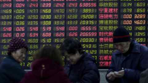Investors stand in front of an electronic board showing stock information at a brokerage house in Shanghai
