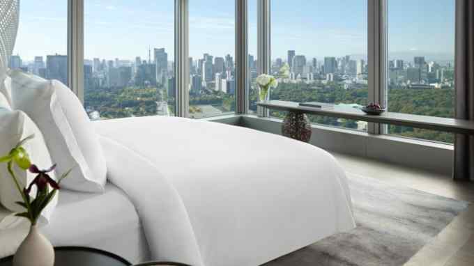 A room in the Four Seasons Hotel Tokyo at Otemachi, with a large white bed overlooking the city through floor-to-ceiling windows