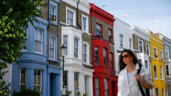A woman in sunglasses walks past a row of colourfully painted houses in London’s Notting Hill