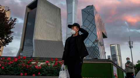 A man wears a protective mask as he walks by the skyline of Beijing’s central business district