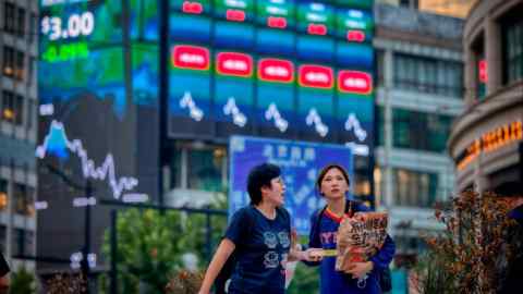 People walk in front of a large screen showing the latest stock exchange data in Shanghai, China