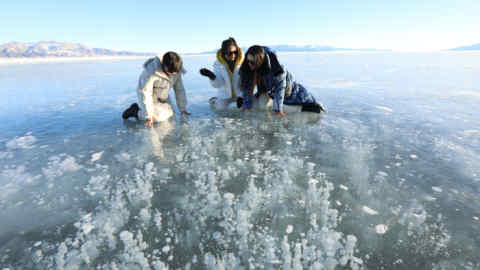 People dressed in snowsuits kneel to look at methane bubbles frozen in the ice in a lake in China