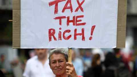 A female protester holding a sign saying ‘Tax the rich’