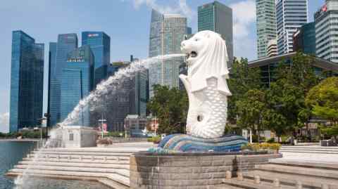 A fountain shaped like a sea dragon sprays water into the river at Merlion Park with Singapore city skyline in the background