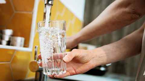 A woman fills a glass with filtered water from a sink