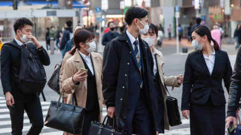 Office workers wearing face masks walk towards the train station in Shibuya, Tokyo