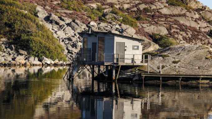 small wooden sauna hut jutting out on to a lake in front of rocks